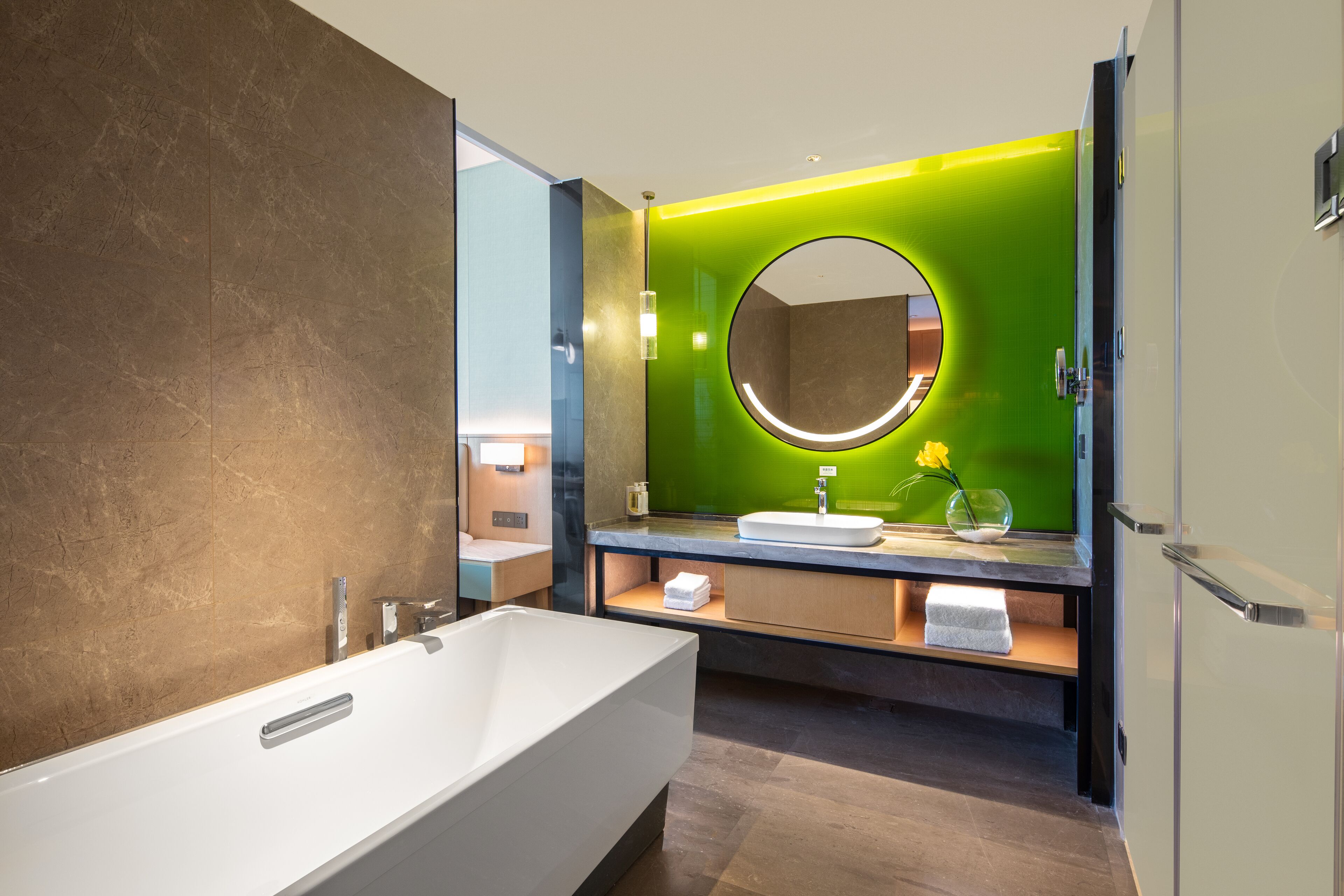 A modern bathroom with a large bathtub, a round mirror, and a green accent wall.