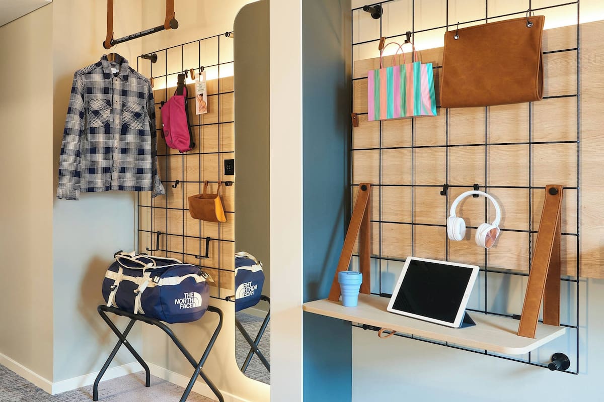 A room with a bed, a bedside table, and a wall-mounted shelf with a laptop and headphones.
