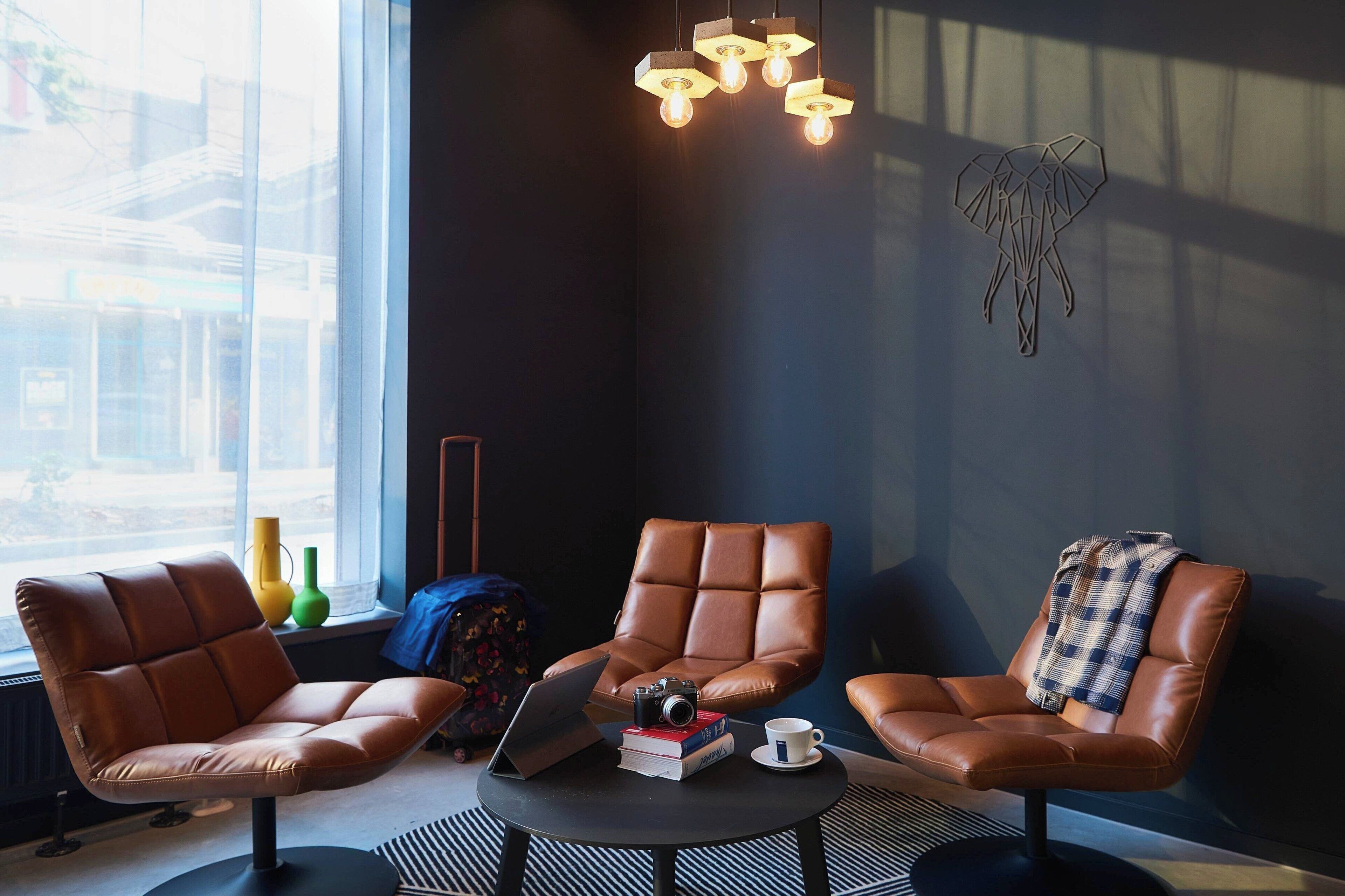 A modern lounge area with leather chairs, a laptop, books, and a camera on a small table.