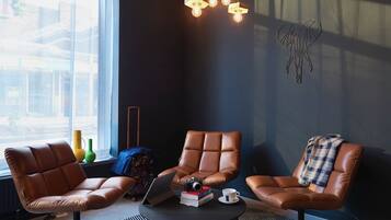 Un espace détente moderne avec des fauteuils en cuir, un ordinateur portable, des livres et un appareil photo posés sur une petite table.