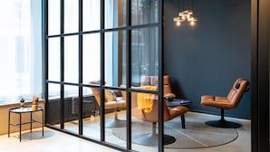 Una habitación moderna con ventanas amplias, sillones de cuero, una pequeña mesa y una lámpara de pared original.