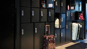 A row of black lockers with keys, a floral suitcase, and a white suitcase against the wall.