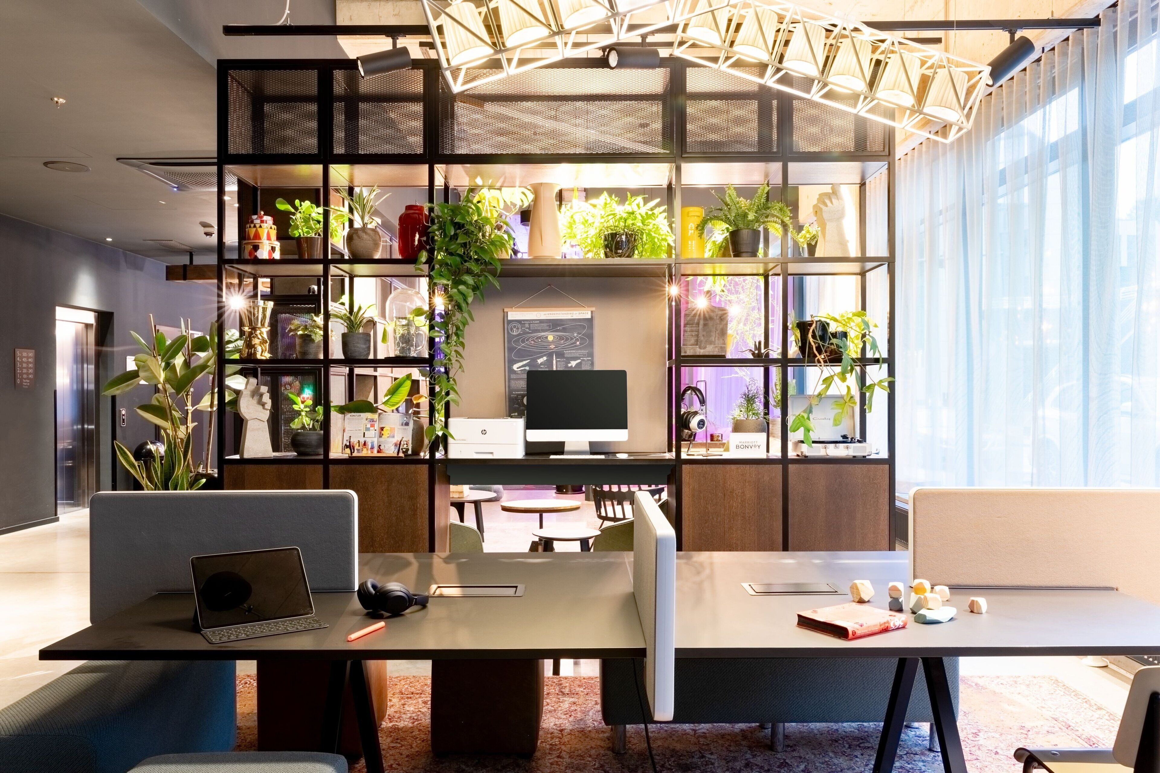 A modern office space with a central desk, multiple seating areas, and a large window with sheer curtains.
