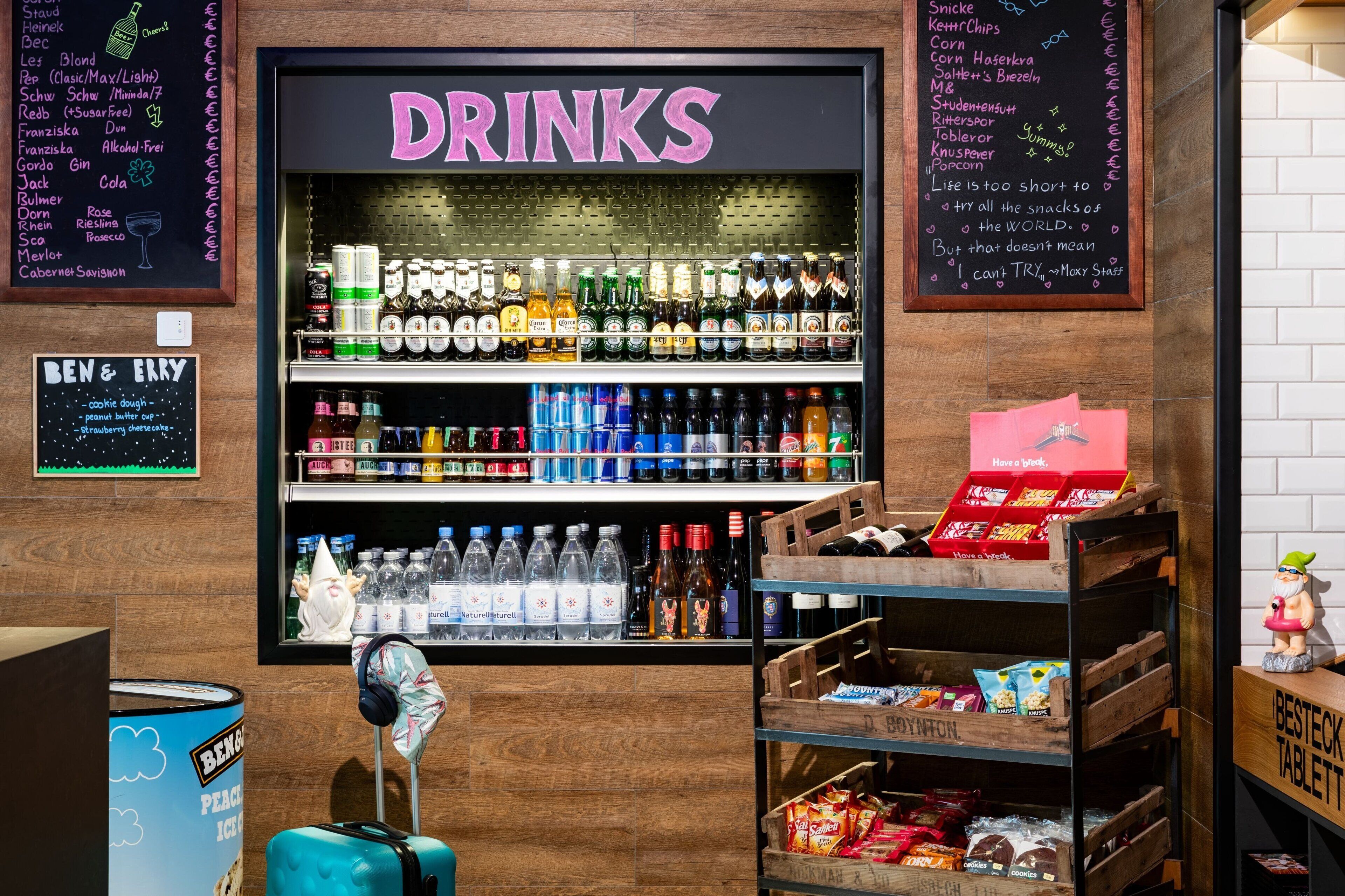 Een drankgedeelte met diverse flessen en blikjes, een krijtbordmenu en een kleine dwergdecoratie.