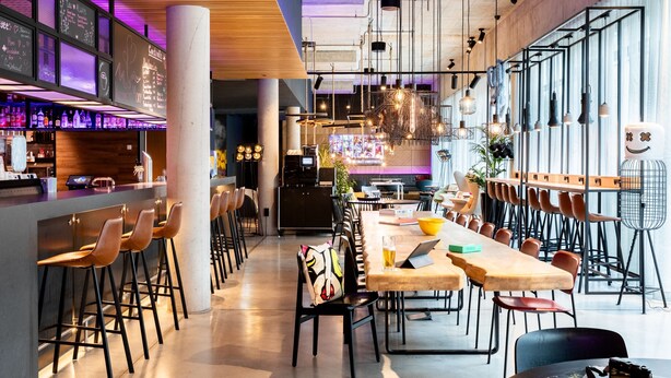 Zona de bar moderna con taburetes altos, una mesa grande para compartir y una barra con botellas.