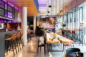 Eine moderne Bar mit hohen Hockstühlen, einem langen Gemeinschaftstisch und einer Bar, an der Flaschen stehen.