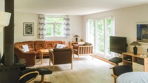 A cozy living room with a brown leather sofa, a wooden coffee table, a small wooden side table, a television, and a lamp.
