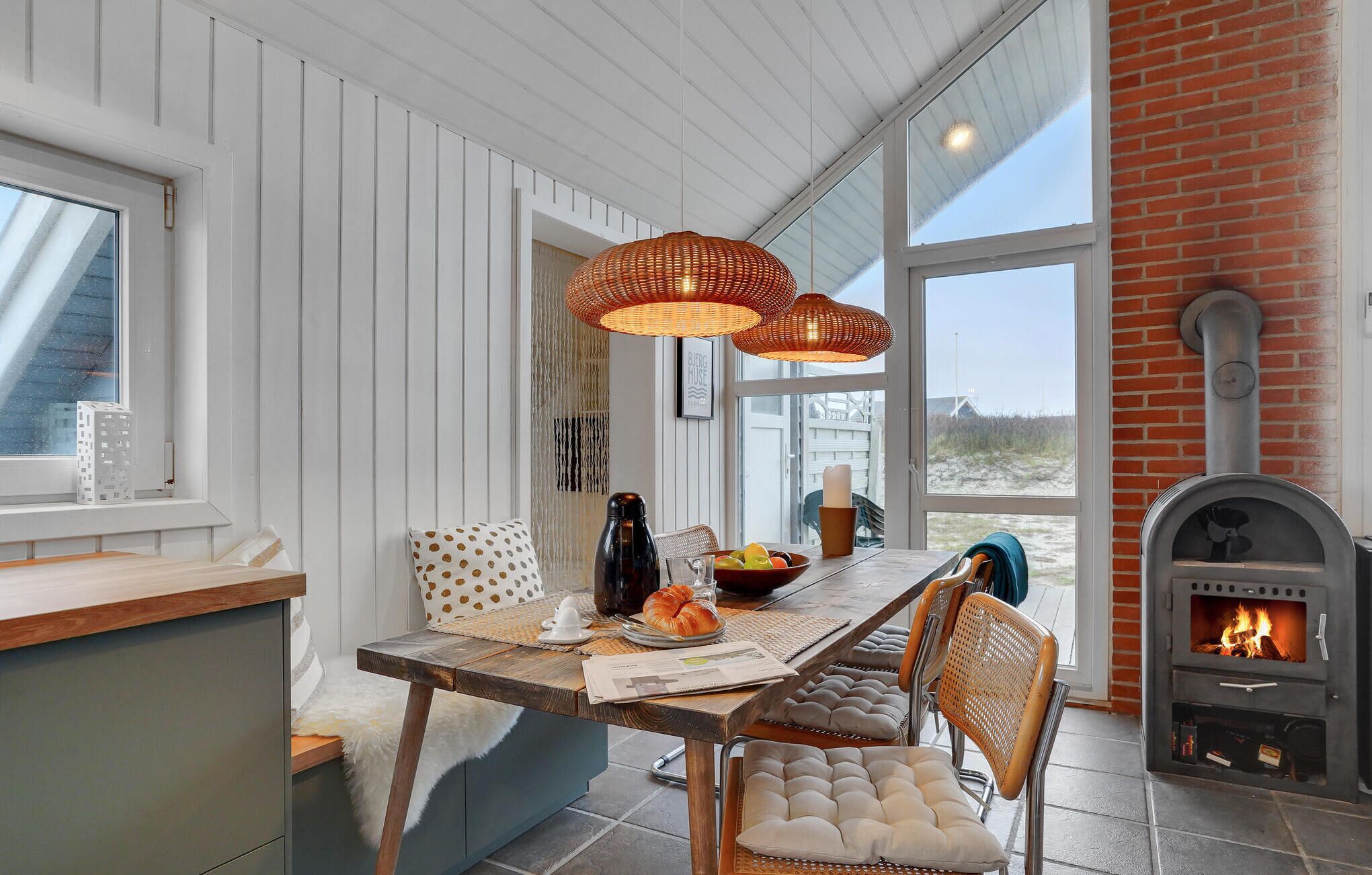 Un coin repas chaleureux avec une table en bois, des chaises en osier et une cheminée en briques.