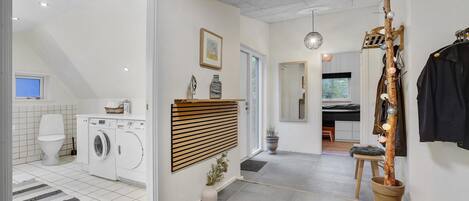 Een moderne wasruimte met een wasmachine en droger, een houten paneelkast en een potplant.