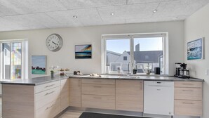 Une cuisine moderne dotée d’un grand îlot central, d’appareils électroménagers intégrés et de grandes fenêtres offrant une vue sur l’extérieur.