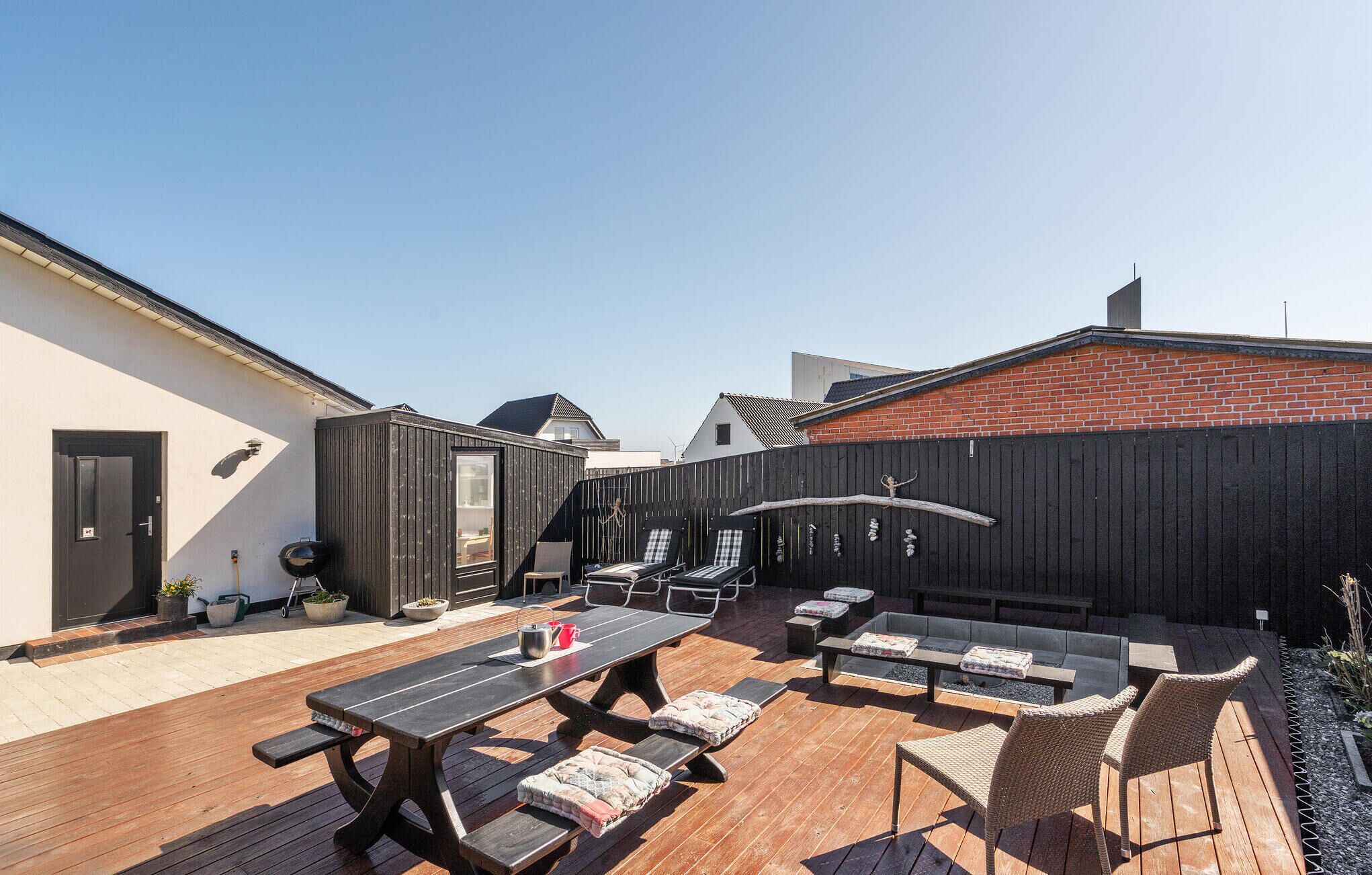Une terrasse avec des meubles en bois, un barbecue et une clôture noire.