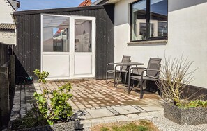 A patio with a table and chairs, a small garden, and a building with a white door and windows.
