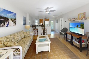 Sala de estar com sofá, mesa de centro, televisão e vista para a cozinha.