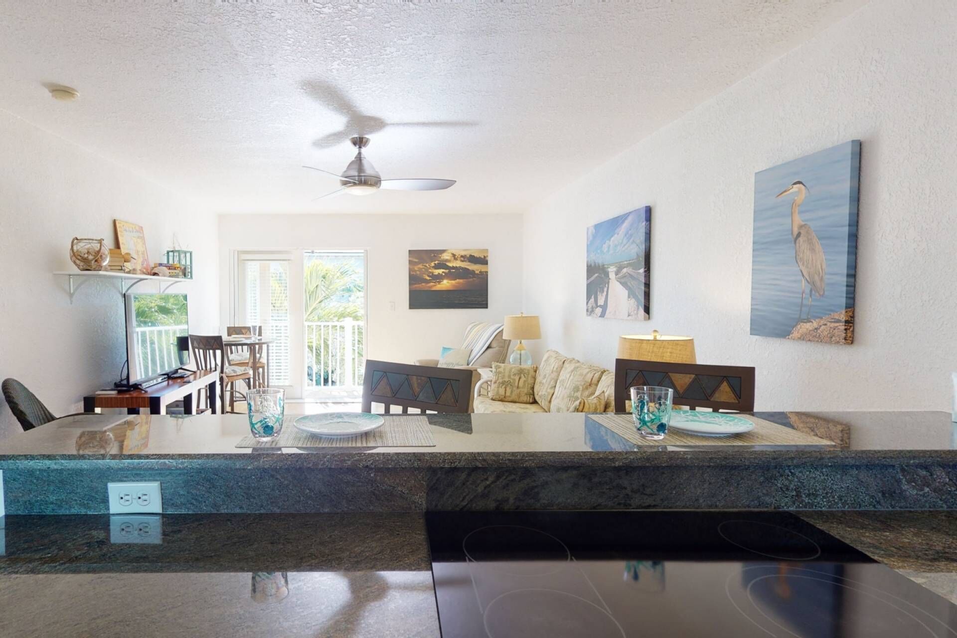 A modern kitchen with a central island, dining area with chairs, and a ceiling fan.