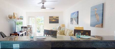 A modern kitchen with a central island, dining area with chairs, and a ceiling fan.
