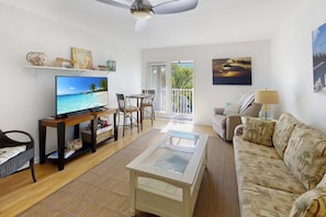 A living room with a television, a sofa, a coffee table, and a balcony with a view. - Walk to The Best Restaurants, Beaches, and Activities. Heated Pool. Fabulous Location. (St. Pete Beach)