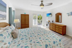 Quarto com cama, cômoda, televisão e porta para varanda.