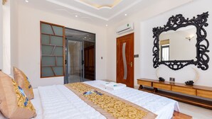 Habitación de hotel con una cama grande, un aparador de madera, un espejo y un cristalero corredizo que da al baño.