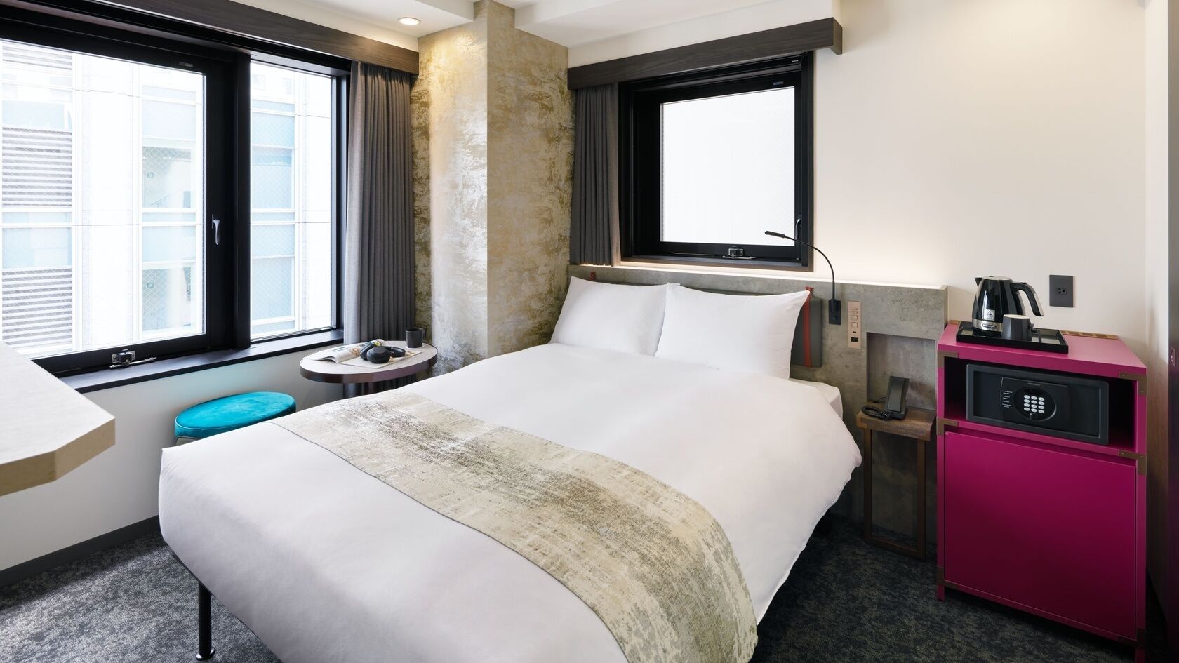 A hotel room with a large bed, a desk, a small round table, a minibar, and a window with curtains.