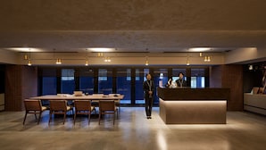 A modern hotel lobby with a reception desk, a large conference table with chairs, and a brick accent wall. - the b ginza (Tokyo)