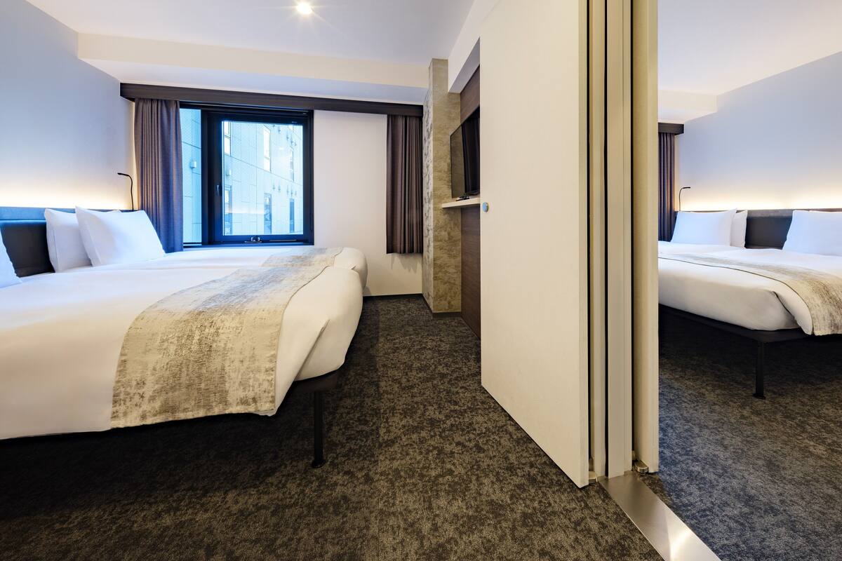 A hotel room with two beds, a large window, and a mirror.