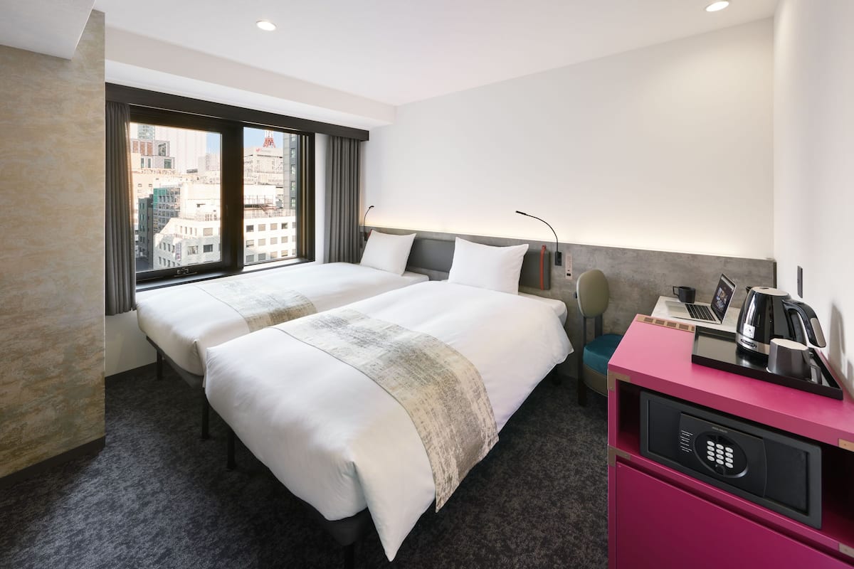 A hotel room with two beds, a desk with a laptop, a coffee maker, and a minibar.