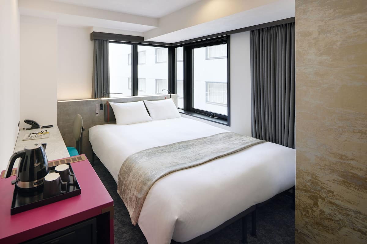 A hotel room with a bed, a desk with a coffee maker, and a window with curtains.