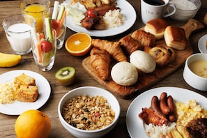 Enjoy a hearty breakfast spread with scrambled eggs, sausages, pastries, cereal, and fresh juice.