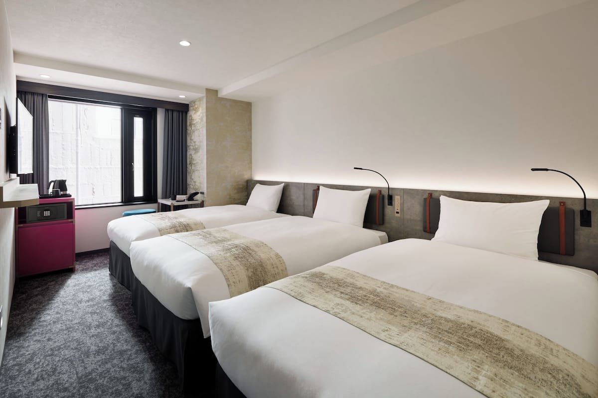 A hotel room with two beds, a desk, a chair, and a large window.