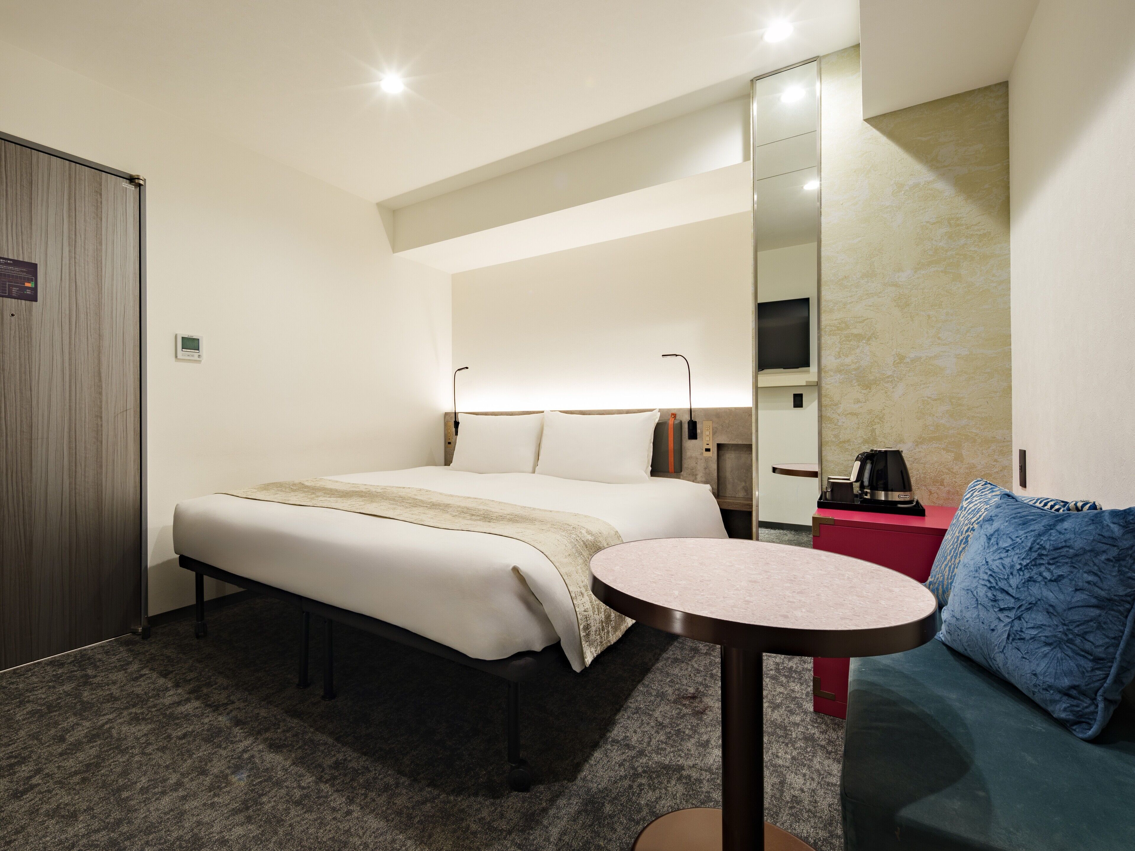 A hotel room with a bed, a small round table, a sofa, a TV, and a mirror.