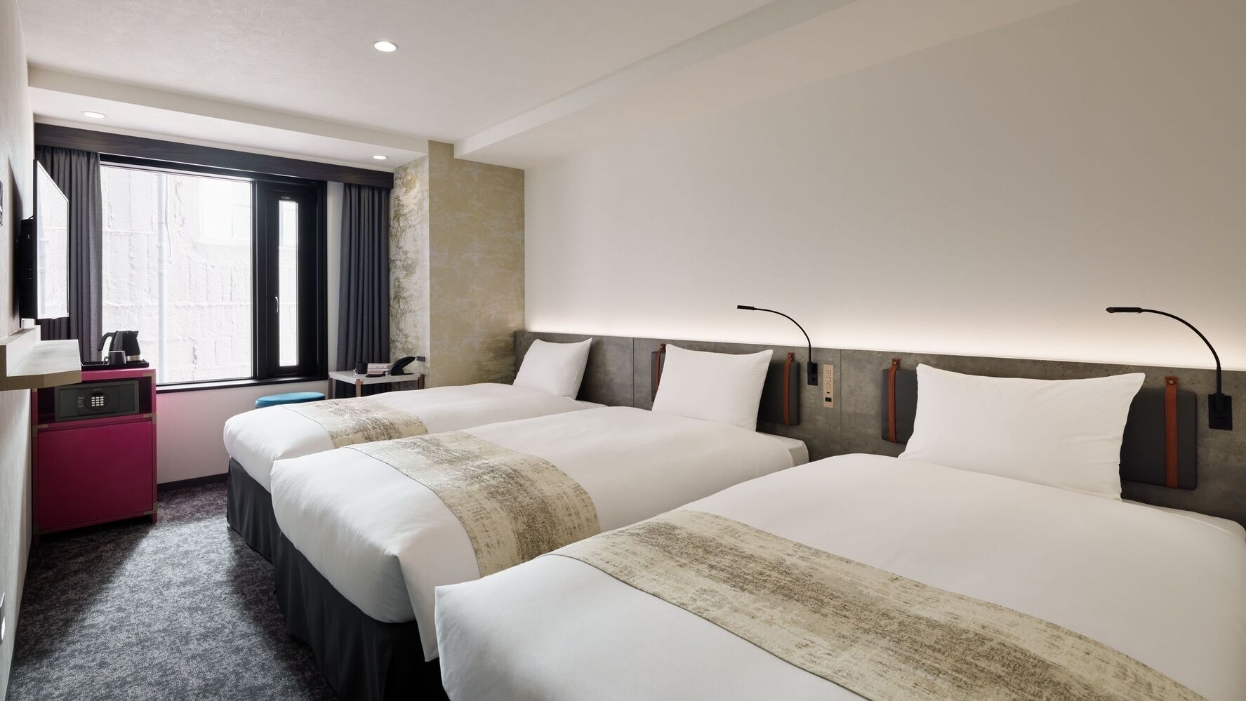 A hotel room with two beds, a desk, a chair, a coffee maker, and a window with curtains.