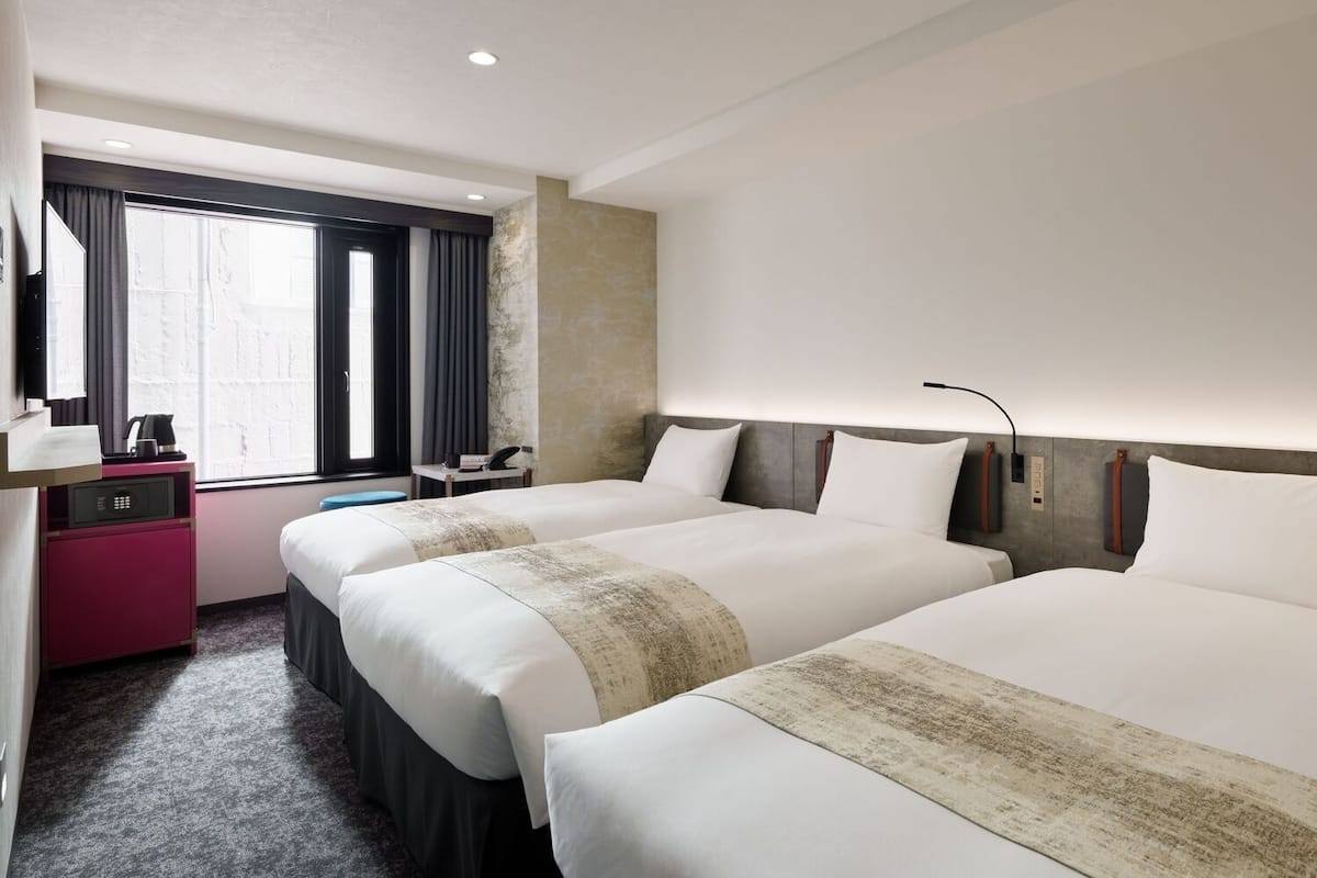 A hotel room with two beds, a desk, a chair, a coffee maker, and a window with curtains.