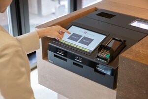 A self-service kiosk with a touchscreen interface for check-in or check-out, a card reader, and a phone.