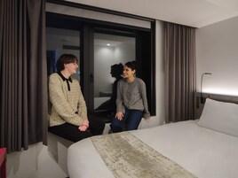A hotel room with a large bed, a window with curtains, and a nightstand.