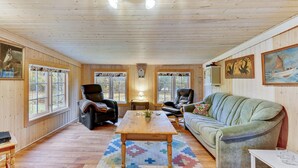 Ein gemütliches Blockhaus-Interieur mit Holzwänden, einem grünen Sofa, zwei Ledersesseln, einem Holztisch und einem gemusterten Teppich.