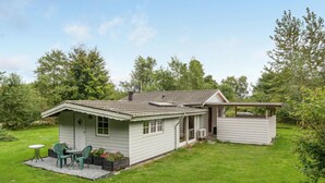 Ein eingeschossiges Haus mit überdachter Veranda, einer kleinen Garage und einem Vorgarten mit Tisch und Stühlen.