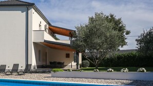 Ein modernes, zweistöckiges Haus mit Swimmingpool, Sitzgelegenheiten im Freien und einem großen Baum.