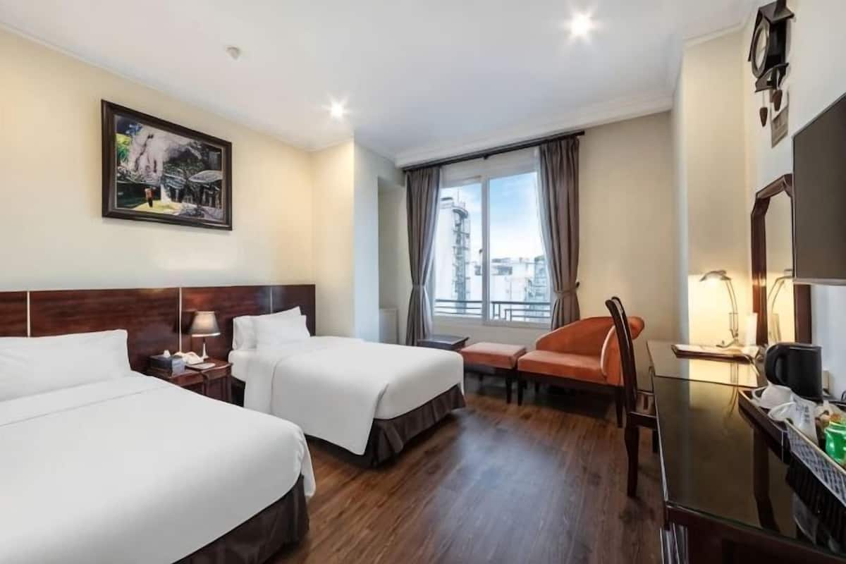 Habitació d'hotel amb dos llits, una taula de nit, una cadira, una finestra amb cortines i vista a la ciutat.