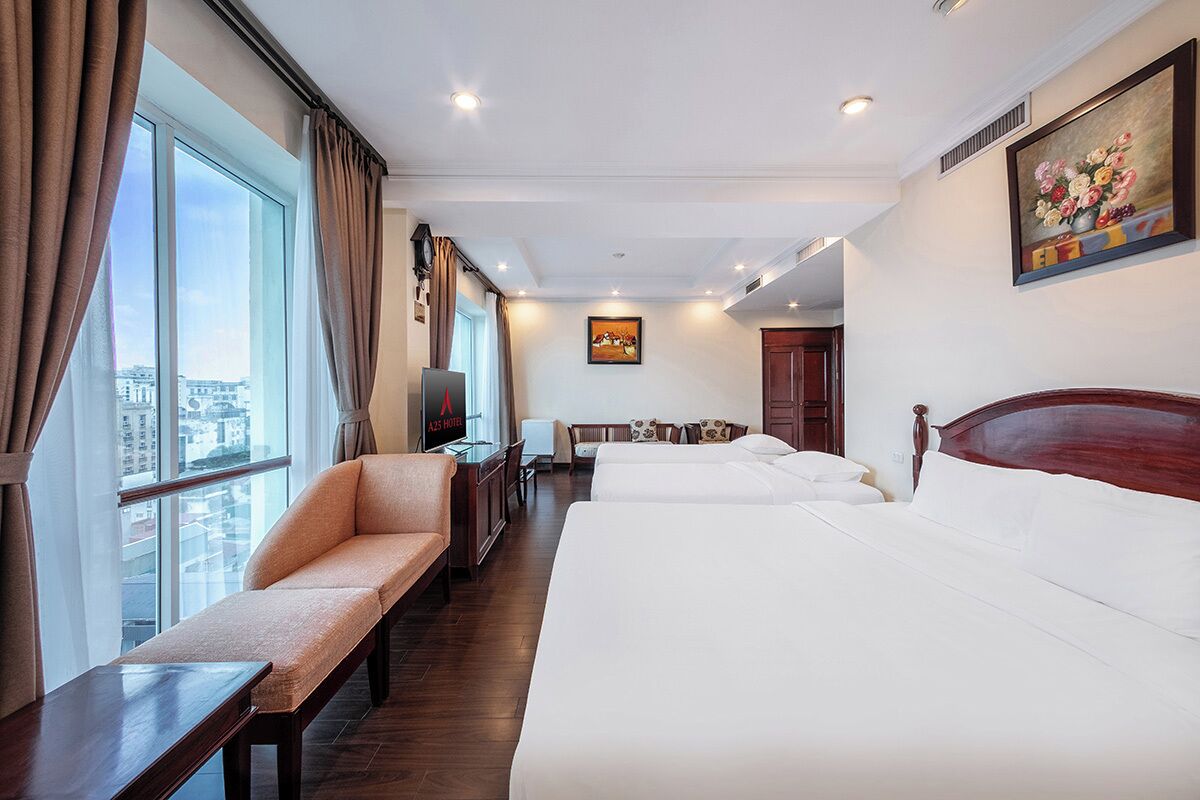 A hotel room with a large bed, a sofa, a desk, and a TV. There is a painting on the wall and a window with curtains.
