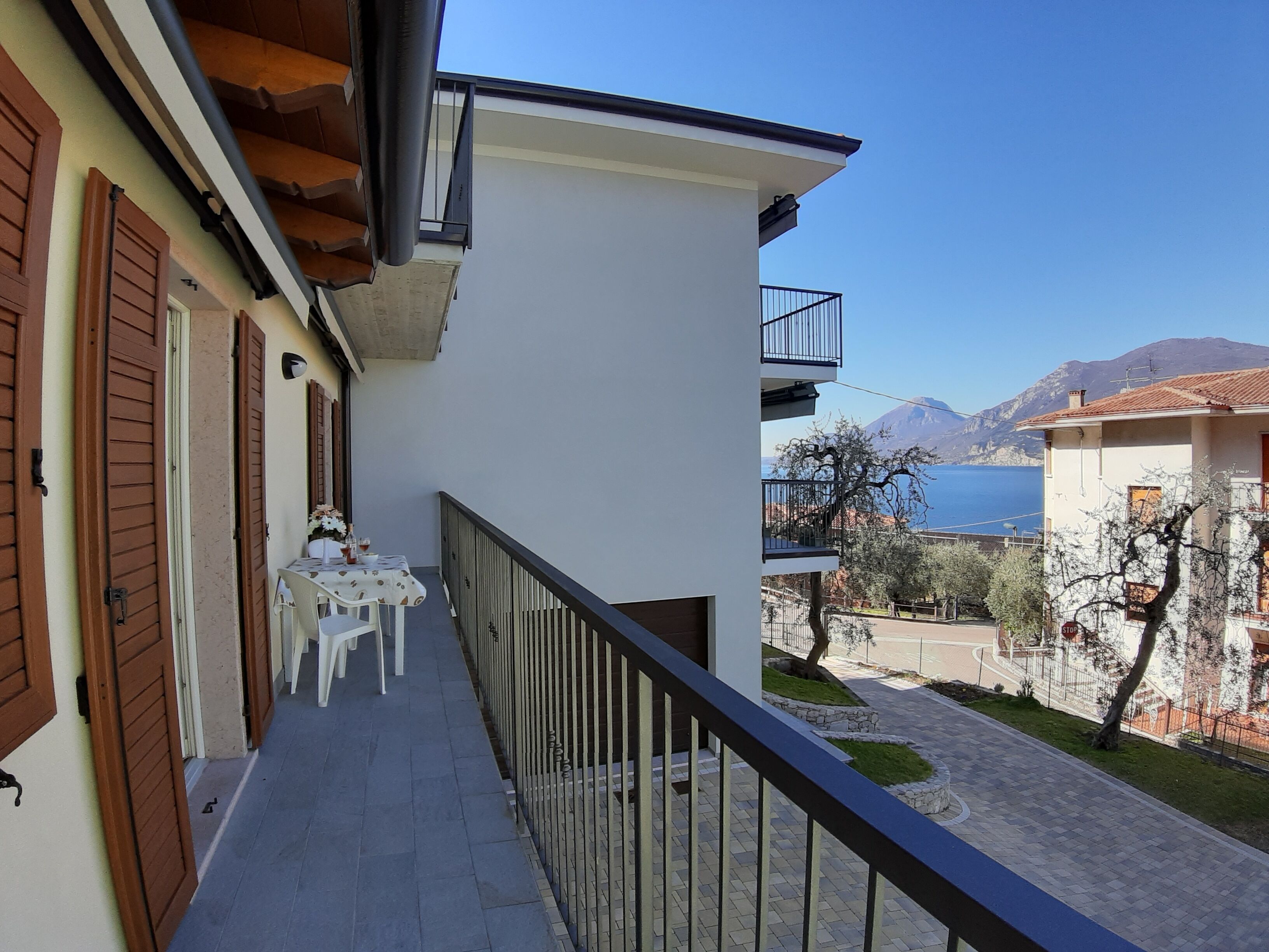 A balcony with a table and chairs, overlooking a coastal area with buildings and a mountain in the background.
