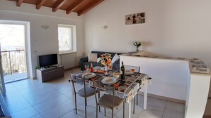 Ein Essbereich mit Tisch für vier Personen, einer Couch, einem Heizkörper, einem Fenster und einer kleinen Küchenzeile.