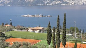 Eine Küstenlandschaft mit einem Tennisplatz, Zypressen und einem Bergpanorama im Hintergrund.