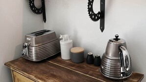 Una kitchenette con encimera de madera, un tostador, un hervidor y una estantería con un tazón, vasos y tazas.