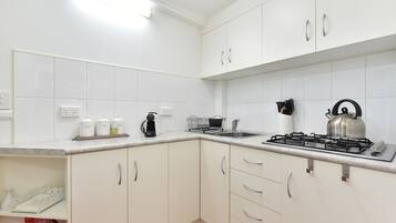 A modern kitchen with white cabinets, a gas stove, a kettle, and a coffee maker.