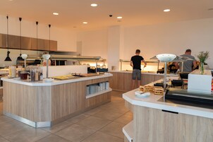 Una cocina moderna con una isla central, iluminación colgante y una persona preparando comida.