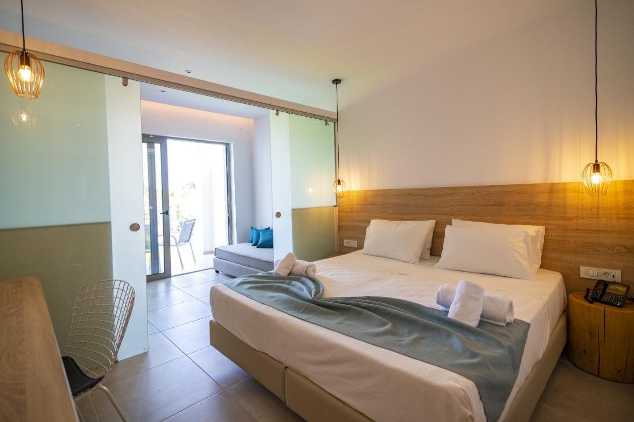 Een hotelkamer met een groot bed, een bureau en een stoel. Er is een houten hoofdbord en een klein nachtkastje met een telefoon.