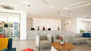 Un hall d’hôtel moderne, doté d’espaces aménagés avec des sièges, d’un comptoir de réception et d’un magasin bien visible où sont exposés divers articles.