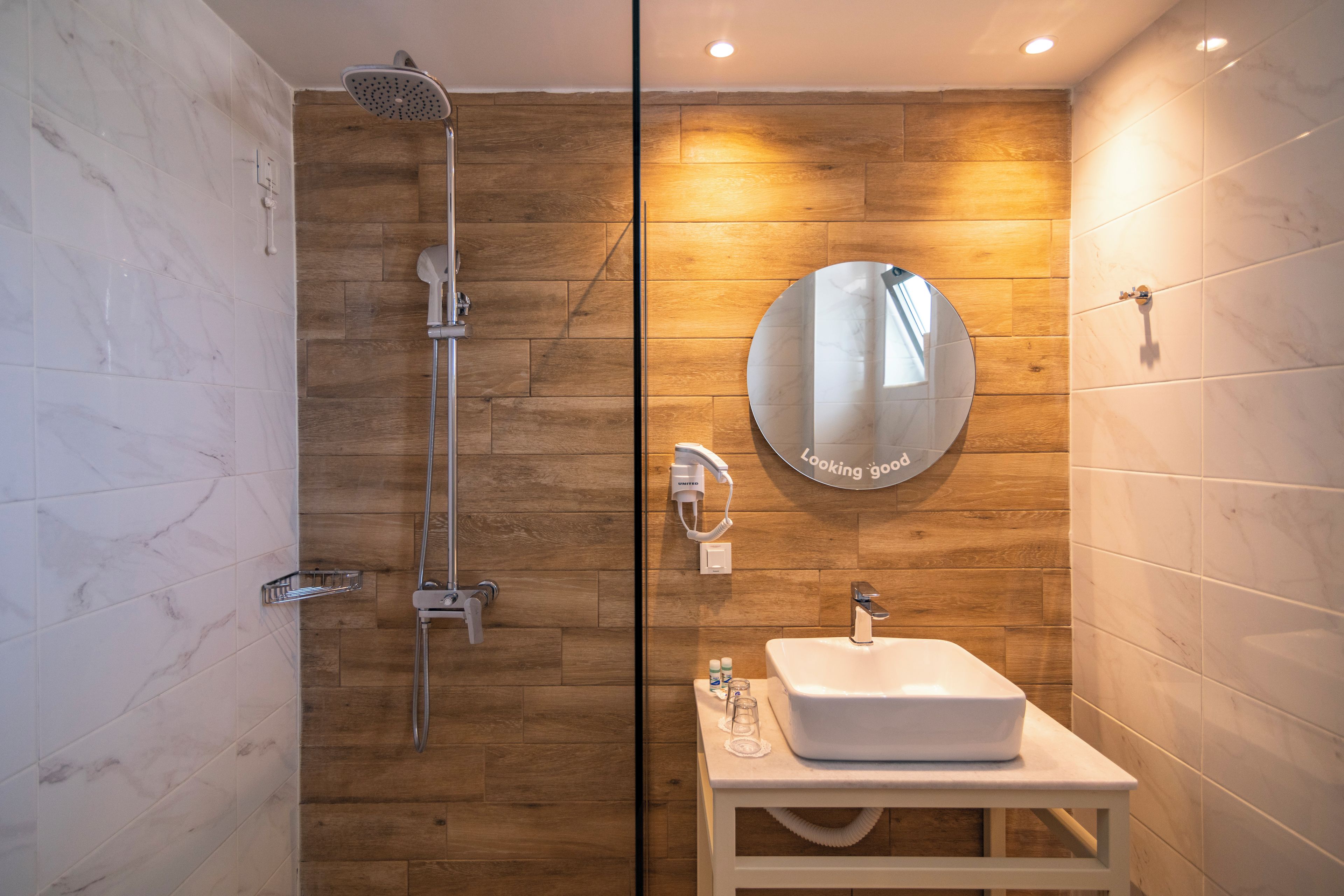 Een moderne badkamer met een glazen douchecabine, een wit wastafelmeubel, een spiegel en een douche.