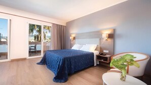 Une chambre d’hôtel avec un lit, une table de chevet, une lampe et une vue sur les palmiers par la fenêtre.