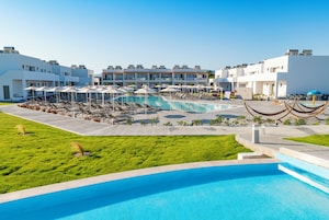 Zona de piscina con sillas de descanso y sombrillas, rodeada de edificios modernos con balcones.